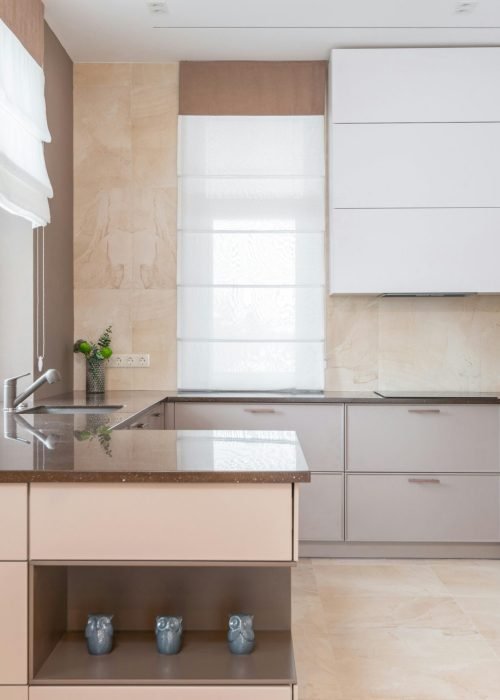 Empty contemporary kitchen with beige walls and light floor tile furnished with minimalist cupboards with gray panels equipped with oven and built in appliances